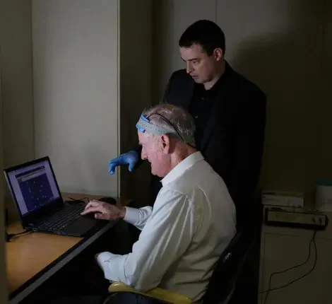 Physician standing next to patient with head equipment doing test on computer