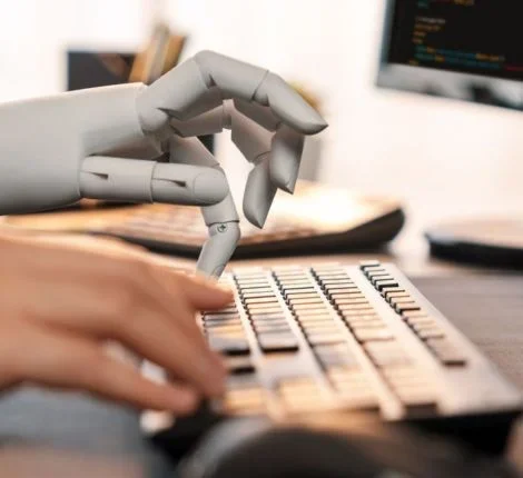 A robotic hand and a human hand type on a keyboard.